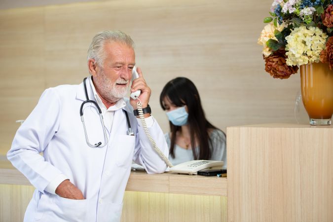 Grey haired doctor on phone in hospital reception area