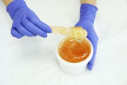 Female hands holding liquid yellow paste for sugaring on blank background, copy space
