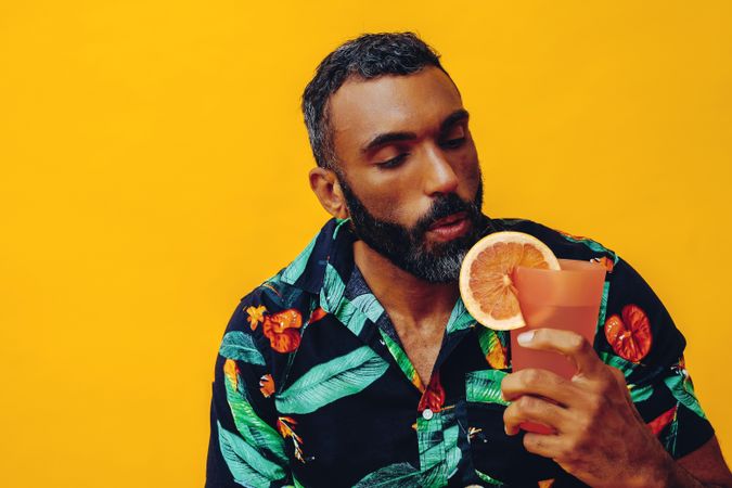 Surprised Black male sitting down with a cocktail in yellow room, copy space