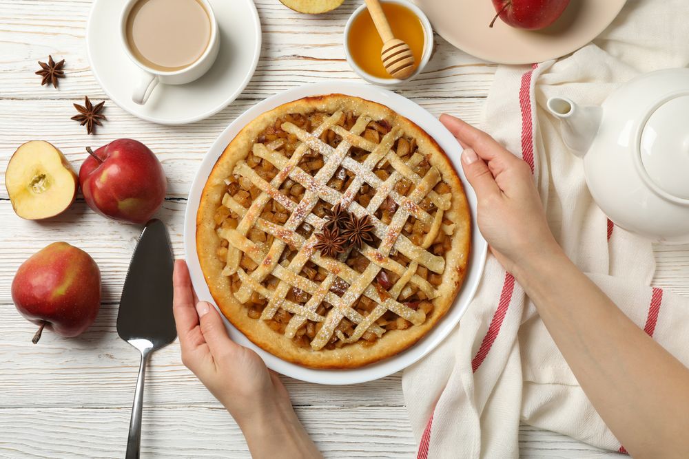 Female hands hold plate with apple pie on wooden background, top view