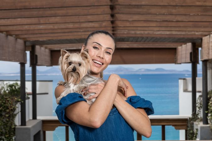 Smiling woman in blue dress holding Yorkshire terrier outdoor