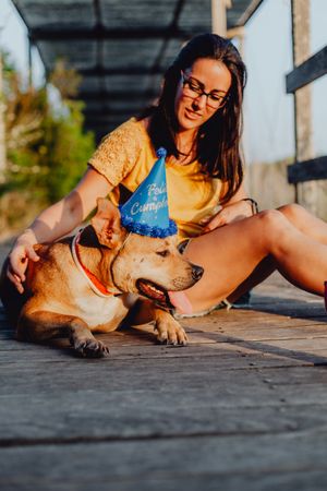 Casual young woman resting next to brown dog with party hat