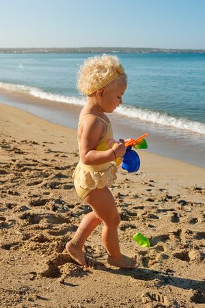Little girl walking with toys on sandy beach