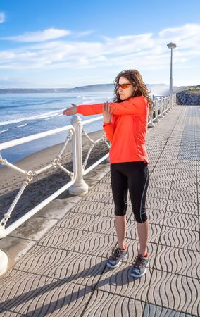 Athletic woman stretching arms before working out on the beach promenade on a summer morning