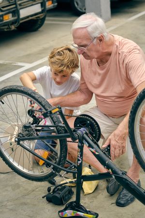 Older man pumping bicycle tire with attentive grandson
