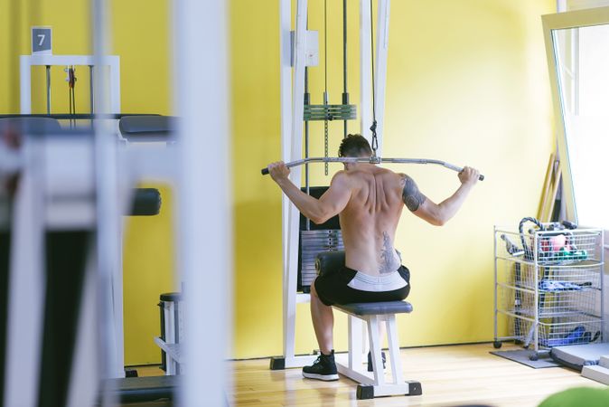 Tattooed male exercising his arms and back on pull down machine