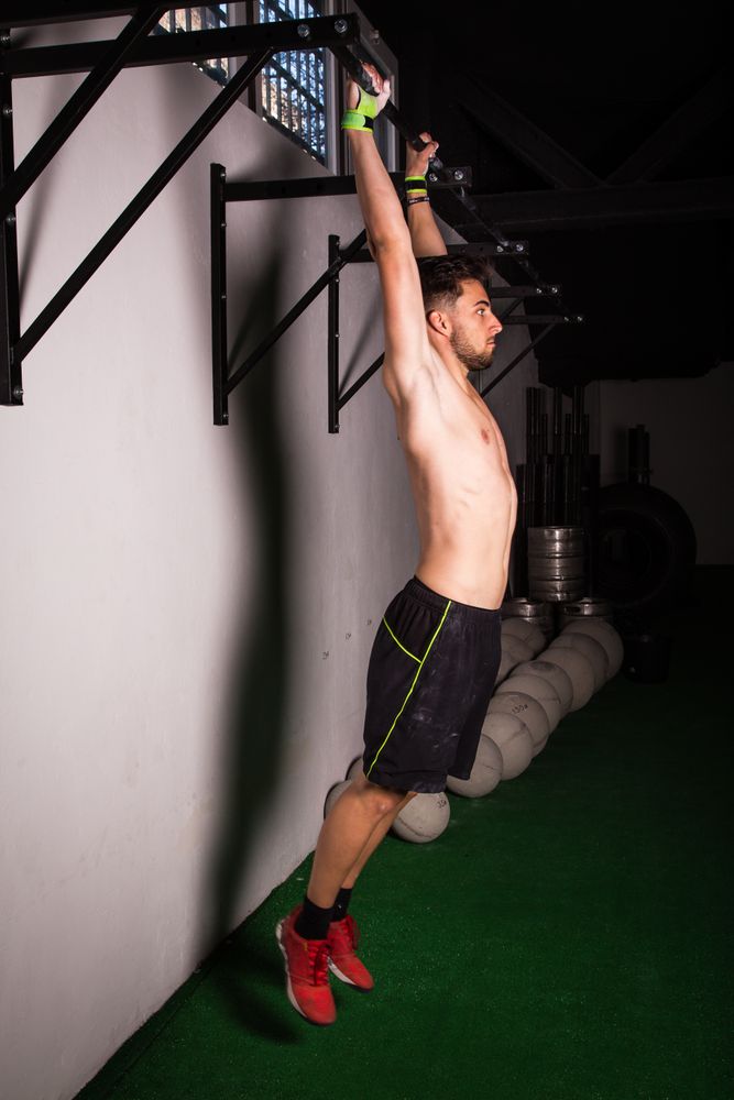 Man hanging on bar near wall in gym