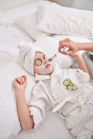 Unrecognizable woman applying facial mask on child