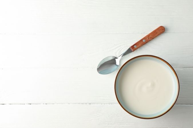 Bowl of sour cream yogurt with spoon on neutral background