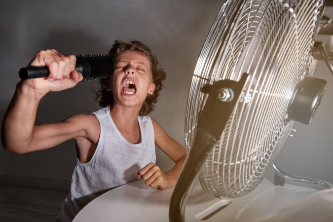Excited preteen boy shouting into comb in front of working fan