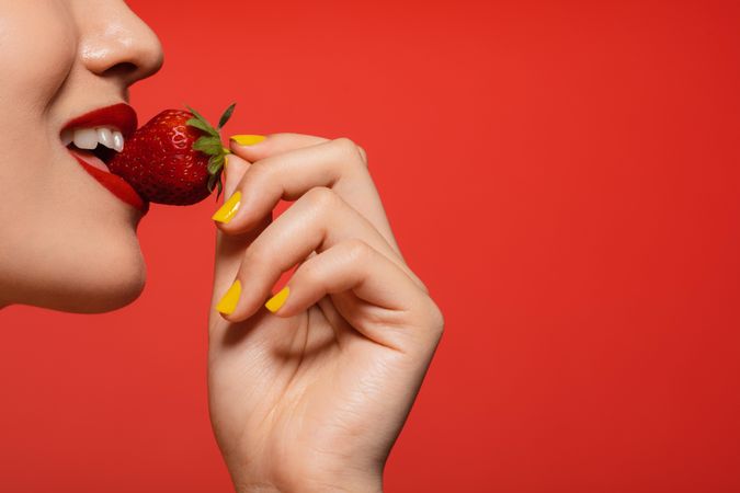 Female biting into a strawberry against a red background