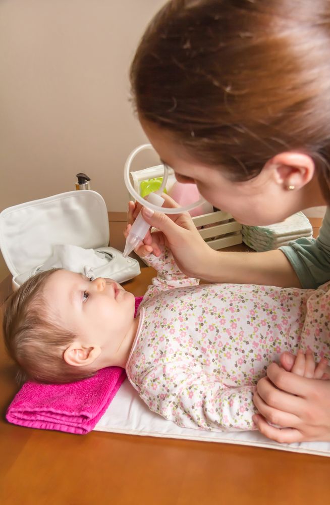 Baby playing with nasal aspirator with mother, vertical