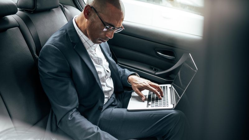 Businessman working on laptop computer while commuting to office in his sedan in back seat