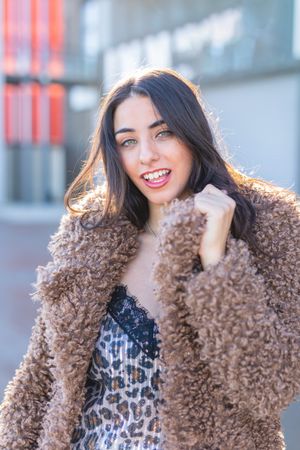 Cheerful woman wrapping in coat on street