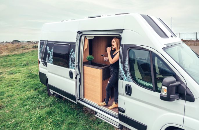 Female on road trip brushing teeth in back of van with door open in the morning