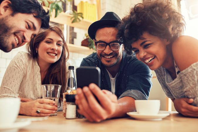 Group of friends sitting together in a cafe looking at mobile phone and smiling
