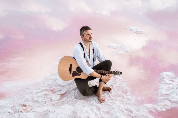 Musician with guitar on pink sandy water