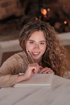 Happy young woman writing in diary at home