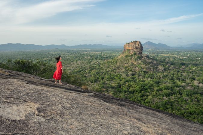 Tourist against solitary rock in middle of green forested plain under clear sky in summer