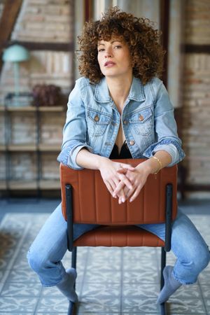 Woman with curly hair sitting on chair reversed with hands in front of her