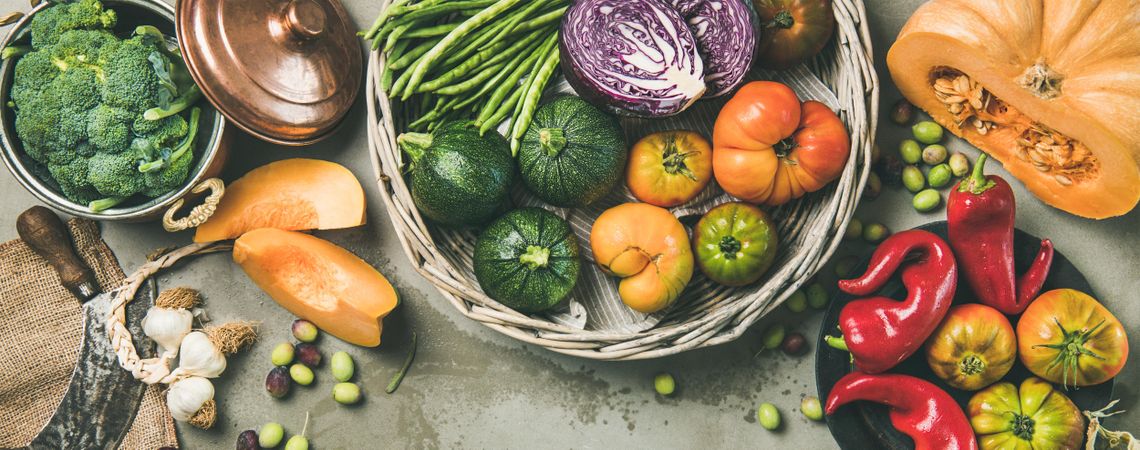 Fresh produce on concrete background, with thatched basket, halved squash, corn, wide composition