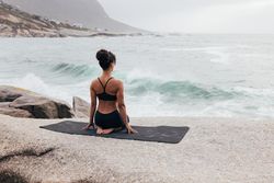Female sitting next to the ocean sitting on knees enjoying the view