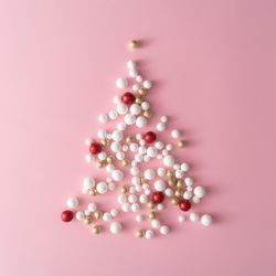 Christmas tree made of gold and red glitter ball decoration on pink background