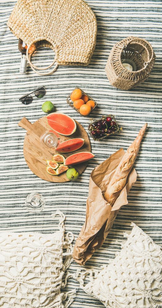 Thatched bag with rose, on picnic blanket with baguette, sliced watermelon and figs