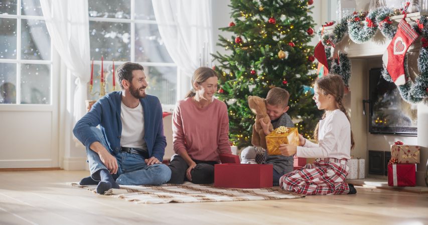 Happy Little Family Exchanging Gifts on Christmas Morning: Brother and Sister Run to Their Parents to Receive their Gifts.