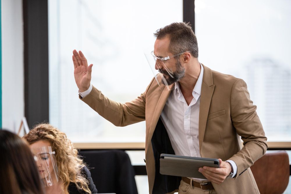 Man in face shield holding digital table with his hand up in office