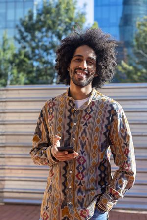 Happy Black man using a mobile phone while standing outdoors on a sunny day