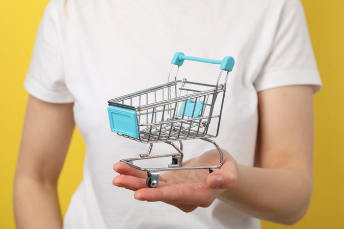 Woman holds shop cart on yellow background, close up