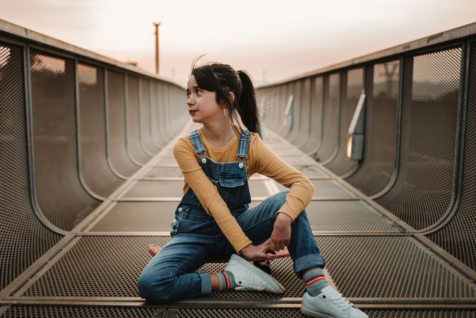 Girl sitting on skateboard on walkway