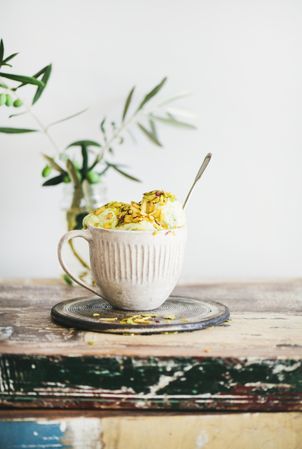 Cup of pistachio ice cream with spoon sticking upright with leaves on light background