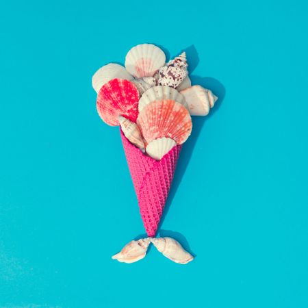 Sea shells in pink waffle cone on bright blue background