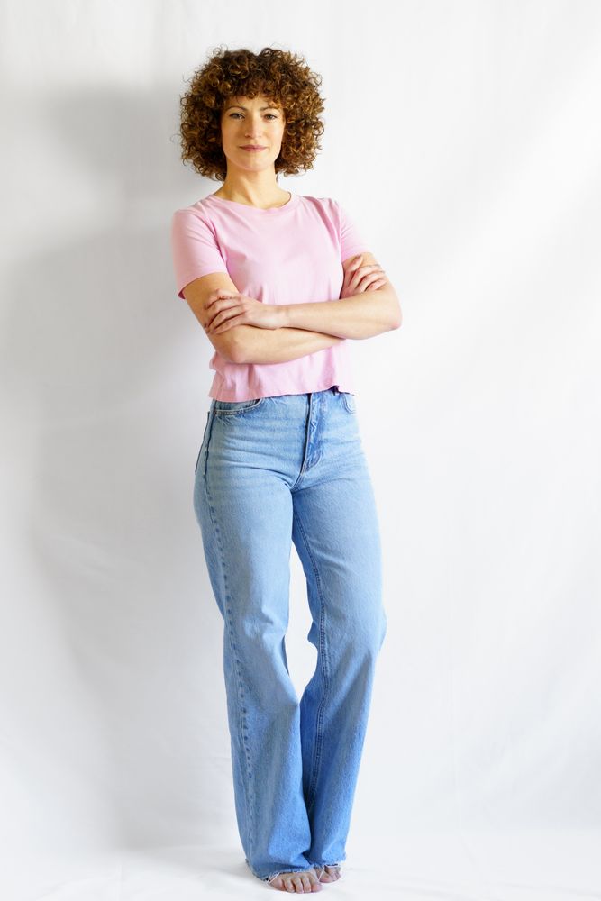 Woman in pink t-shirt and jeans standing barefoot in bright studio