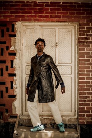 Young man in dark leather coat standing light door
