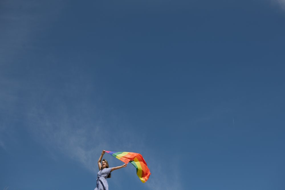 Young woman with rainbow banner against sky
