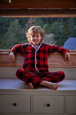 Positive boy sitting on cabinet near window in apartment