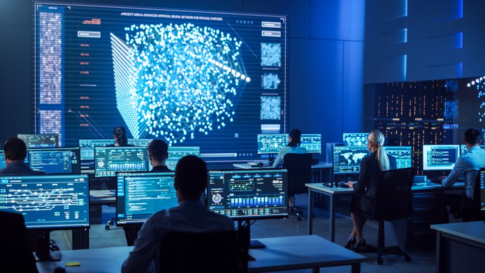 Diverse Team Collaborates in a Futuristic Control Room, Analyzing Data on Multiple Screens to Enhance Cybersecurity and Operational Efficiency.