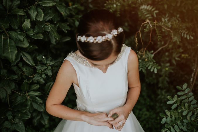 Bride in charming dress admiring finger ring in garden