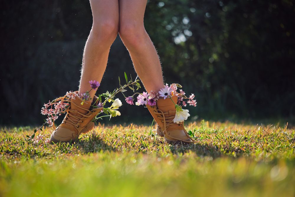 Crop person wearing boots with flowers standing on grassy glade
