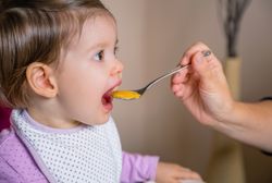 Baby eating puree from a spoon in the hand of mother