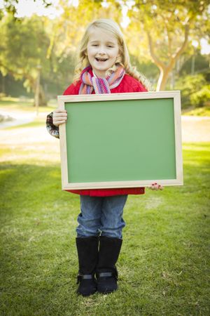 Cute Girl Holding a Green Chalkboard Wearing Winter Coat Outdoors.
