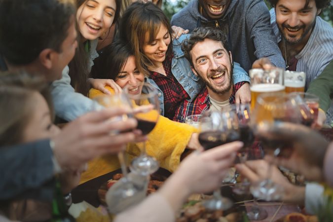 Group of rowdy friends toasting beer and wine around table