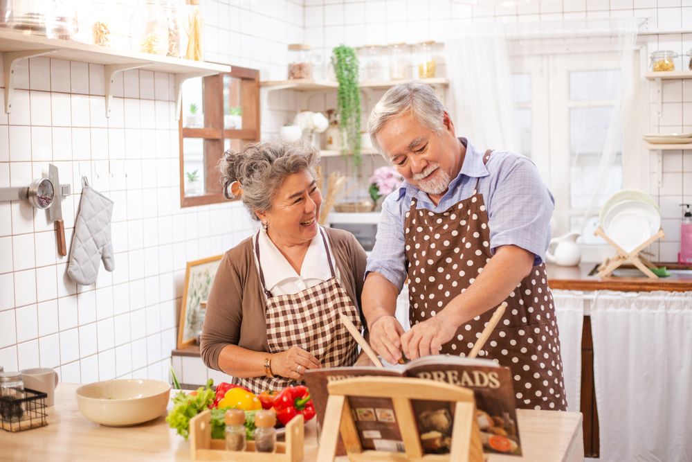 Happy Asian mature couple cooking salad in home kitchen