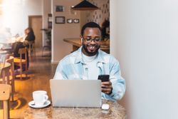 Cheerful Black man browsing smartphone in cafe