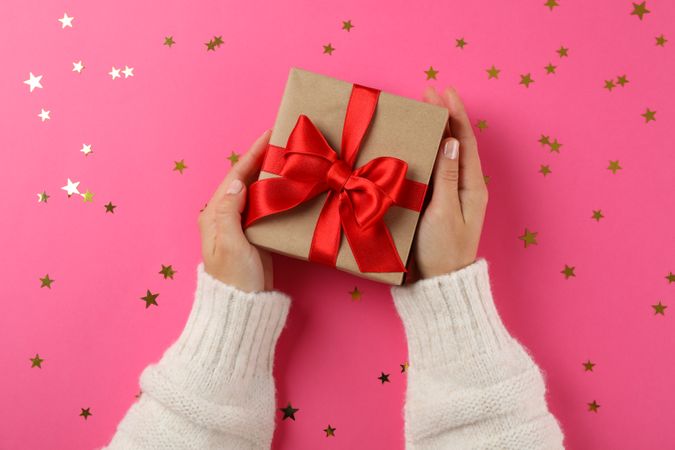 Young woman holding gift box on pink background, space for text