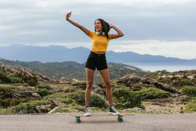 Smiling woman on longboard and taking selfie