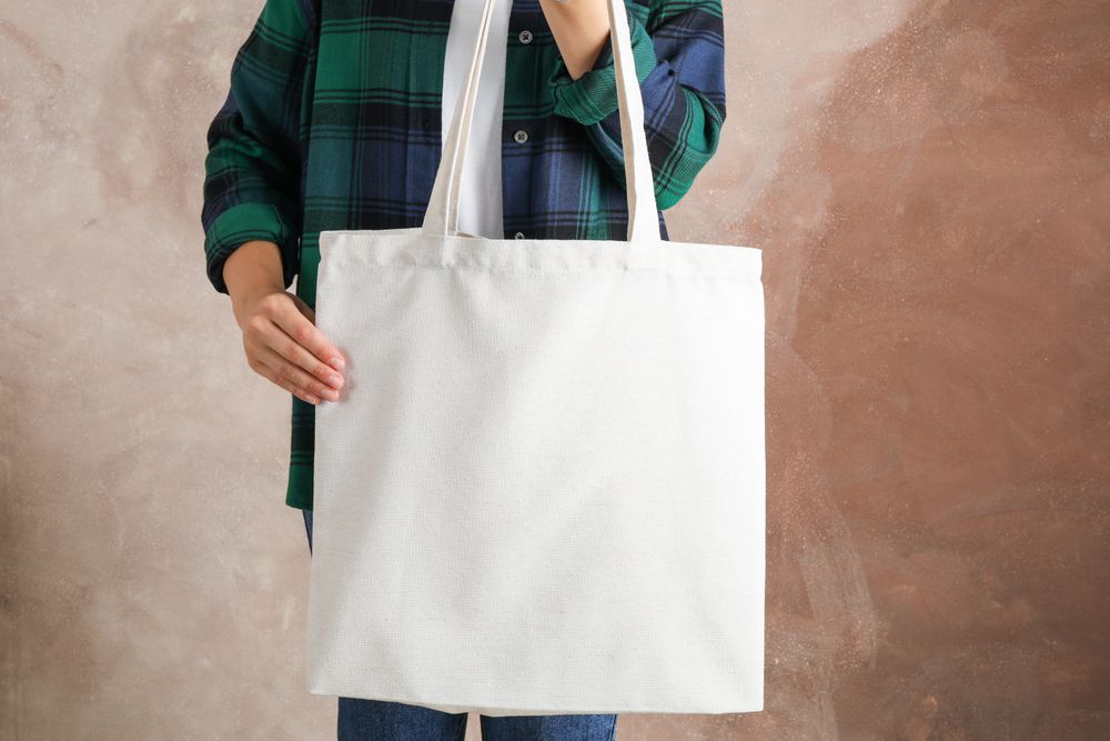 Young woman holding tote bag against brown background, empty space